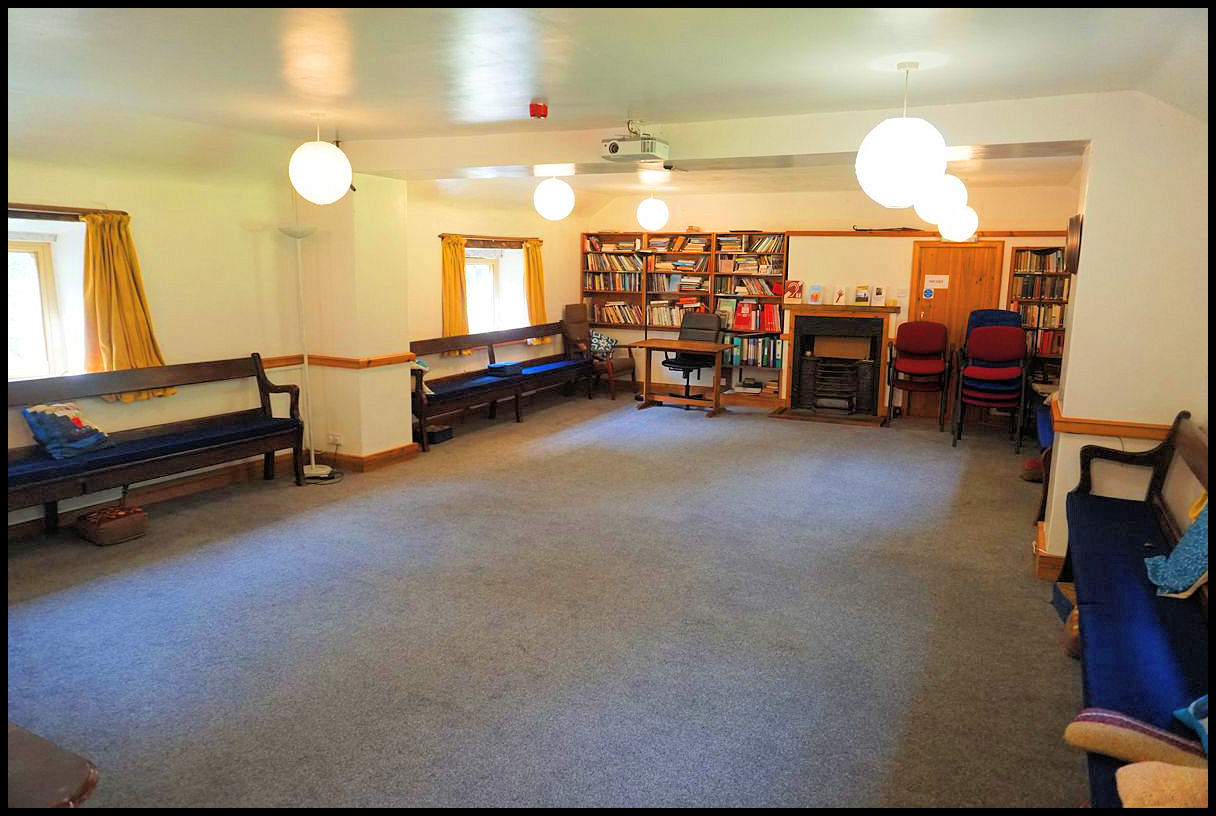 spacious room with church pews against the walls and chairs stacked at one end